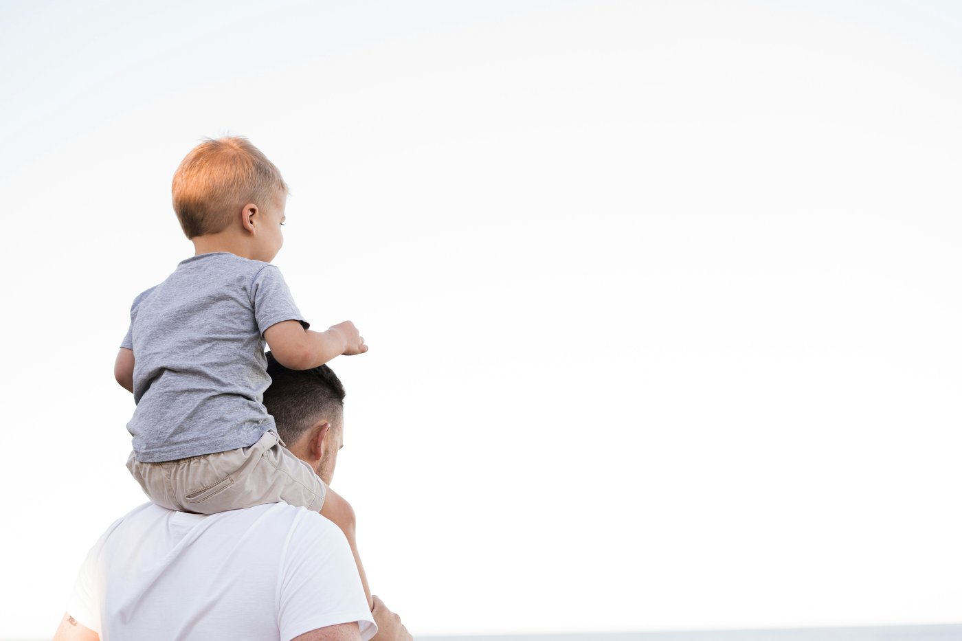Padre cargando a su hijo en los hombros mirando hacia el horizonte